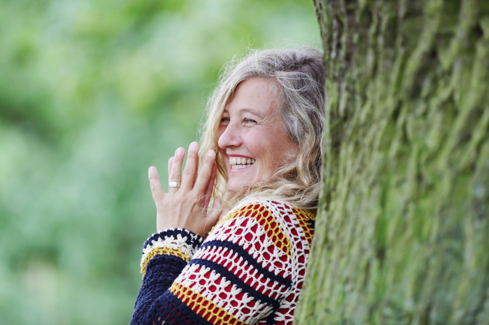 Jutta Fuhse lehnt lachend an einem Baumstamm im Grünen